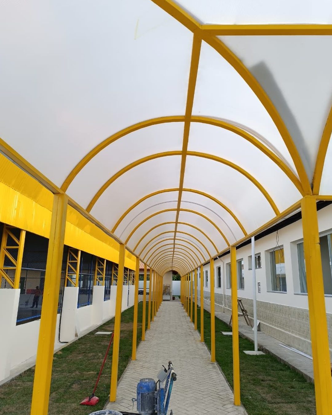 Passarela com cobertura de policarbonato e estrutura amarela na Escola Monsenhor