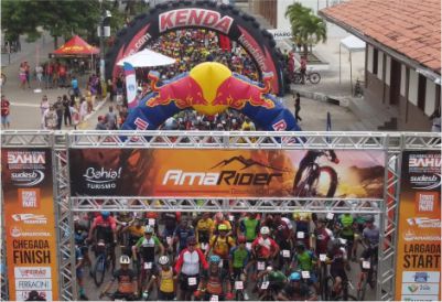 Pórtico oficial do evento Amarider com ciclistas posicionados na largada e estrutura temática ao fundo